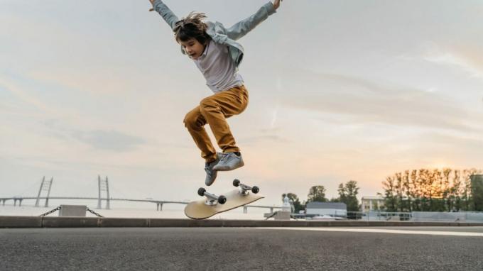 Chlapec skákanie na skateboarde na ulici. Zábavné dieťa korčuliar cvičí ollie na skateboarde pri západe slnka.