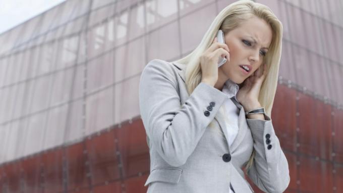 Žena s ADHD, ktorá počúva niekoho na mobilnom telefóne a hnevá sa pred vysokou budovou